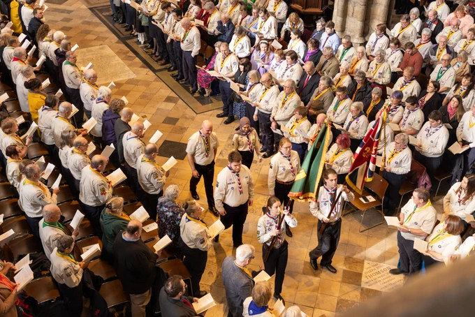 A group of Scouts processing a flag through Westminster Abbey during a service, with members of the congregation standing on either side