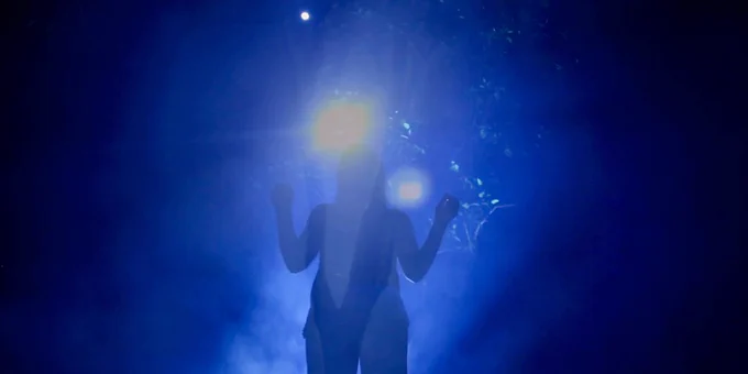 An adult stands in bright light surrounded by dark shadow. The adult is in shadow, and there is blue light outlining the body.