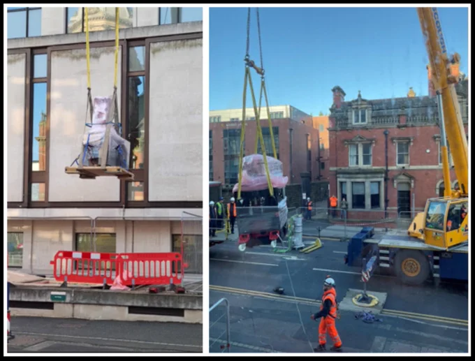 Two heavily wrapped transmission electron microscope columns being lifted out of a basement by a crane