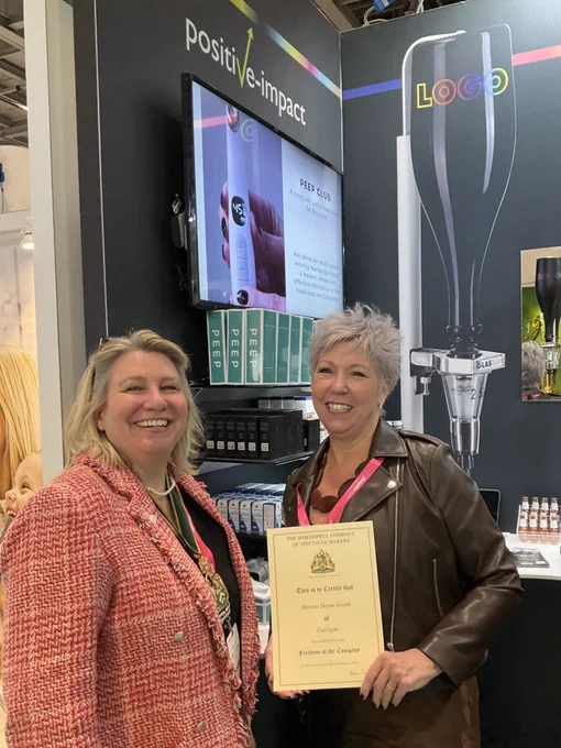 Liz Shilling & Maxine Green at the Positive Impact stand. Max is holding her Freedom Certificate. Both women are smiling broadly.