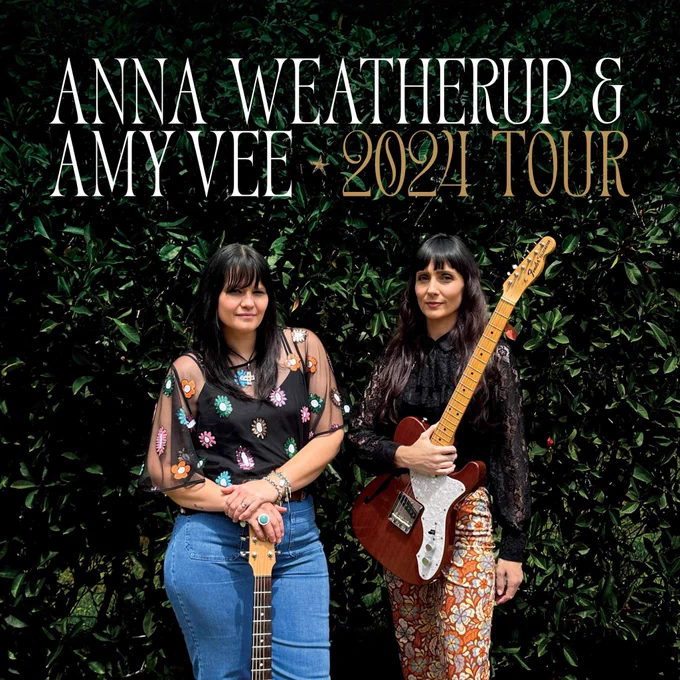 Anna and Amy stand poised with their guitars against a leafy dark green background. Both have a wry smile.