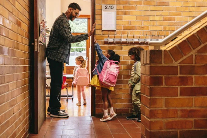 A teacher high fiving a child as they enter a school classroom.