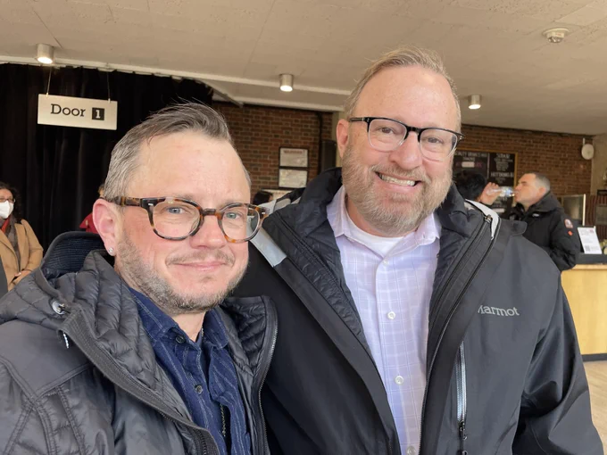 Two people wearing glasses smile and pose for a photo.