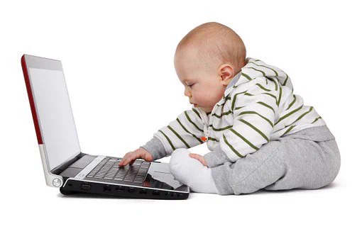 A baby sat on the floor with an open laptop.