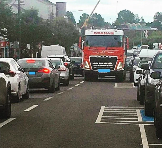 Parking protected cycle lane in Newbridge showing a disability parking bay squeezed in between a busy road with oncoming red quarry truck driving over our access aisle & cycle lane on passenger side with bollards dno safe door space. 