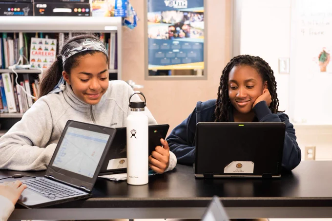 Two young students at a Code Club in the USA sitting at a desk looking at their laptops. 