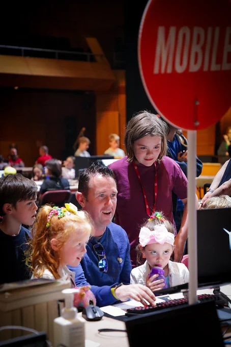 A mentor looking at a computer surrounded by four young creators
