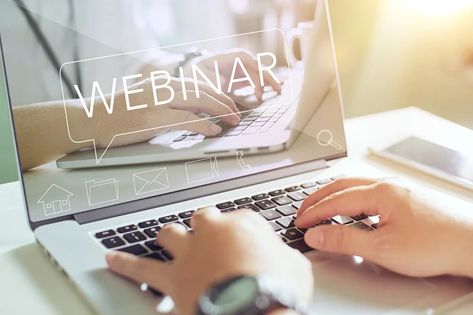 dos manos sobre el teclado de un portátil, en cuya pantalla se lee «webinar»
