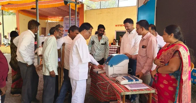 वरील फोटो मध्ये एका ठिकाणी मतदान केंद्रस्तरीय अधिकारी evm  मशीन घेऊन उभे आहेत. त्यांच्या समोर दिव्यांग व्यक्ती उभे आहेत त्यांना मतदान केंद्रस्तरीय अधिकारी evm मशीनची माहिती देत आहे त्यासोबतच प्रात्याक्षिक सुरू आहे. 