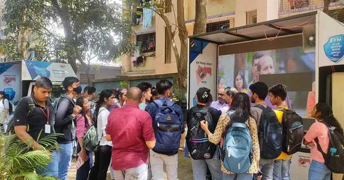 वरील फोटो मध्ये EVM वाहन उभे आहे त्यावर evm मशीनची माहिती देणारे बॅनर लावले आहे आणि त्या वाहन मध्ये LED स्क्रिन लावली आहे त्यावर मतदान जागृतीपर व्हिडिओ चालू आहे. वाहनाच्या भोवती विद्यार्थ्याची गर्दी जमली आहे आणि मतदान केंद्रस्तरीय अधिकारी त्यांना मशीन विषयी माहिती सांगत आहे. 