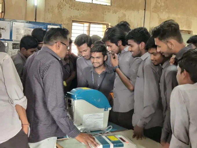 वरील फोटो मध्ये एका ग्रामीण ठिकाणी मतदान केंद्रस्तरीय अधिकारी EVM मशीन घेऊन आहेत त्यांच्या भोवती लोकांची गर्दी जमली आहे. त्यांना ते EVM मशीनची माहिती सांगत आहे सोबतच प्रात्याक्षिक सुरू आहे.