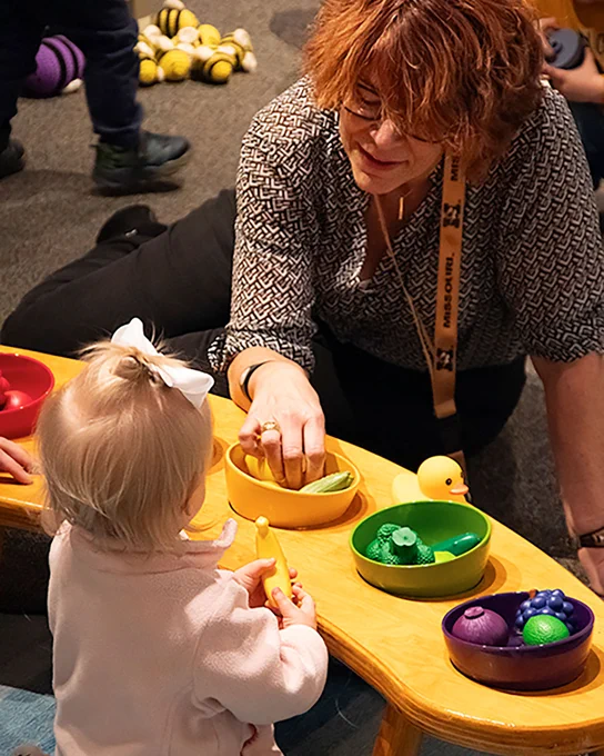 An image of a toddler playing with a woman, sorting colorful play food into bowls.