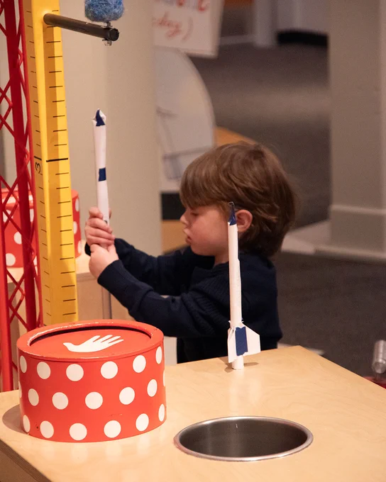 A picture of a young boy playing with paper rockets in 'The Questioneers' exhibit.