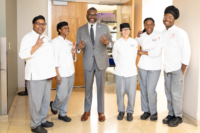 Chicago Mayor Brandon Johnson poses for a photo with a group of people in matching uniforms.