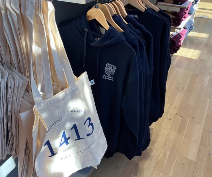 Image showing Fairtrade organic cotton branded tote bags in natural colour and navy hoodies in University of St Andrews shop. 