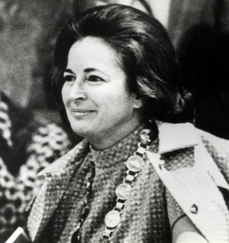 Black and white photo of a smiling woman with dark hair wearing a nice dress and a matching coat over her shoulders.
