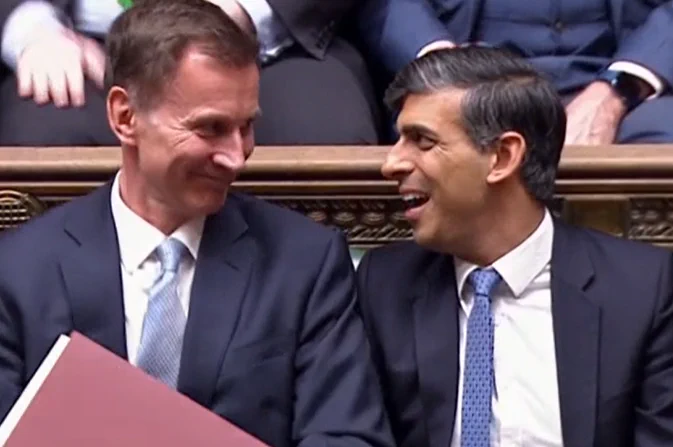 Jeremy Hunt and Rishi Sunak grinning awkwardly at each other in parliament, just after the budget had been delivered.