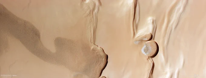 Una veduta rettangolare di terreno color marrone chiaro mostra una serie di caratteristiche di Marte: una fascia increspata di dune di sabbia a sinistra; due argini di rilievo che tagliano il centro della cornice; due ripidi terrapieni semicircolari nel terzo più a destra dell'inquadratura; e infine, terreno liscio a destra. Ci sono segni di terreno stratificato in tutta l'inquadratura e le ripide scogliere proiettano ombre scure sul terreno sottostante. 