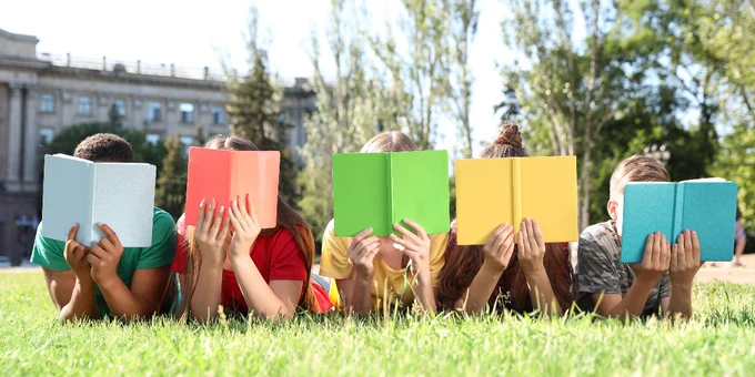 a group of children sitting in the grass, reading books