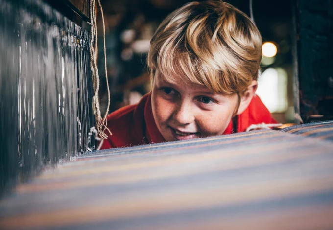 A young boy looking at a blanket being woven. 