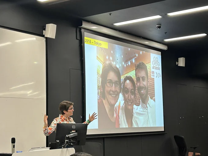 Cathy at a lecturn with an image of the 3 founders explaining how it all began