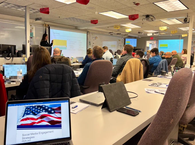 An instructor stands in front of a slide on post timing at the front of a classroom filled with public information professionals in a social media engagement class