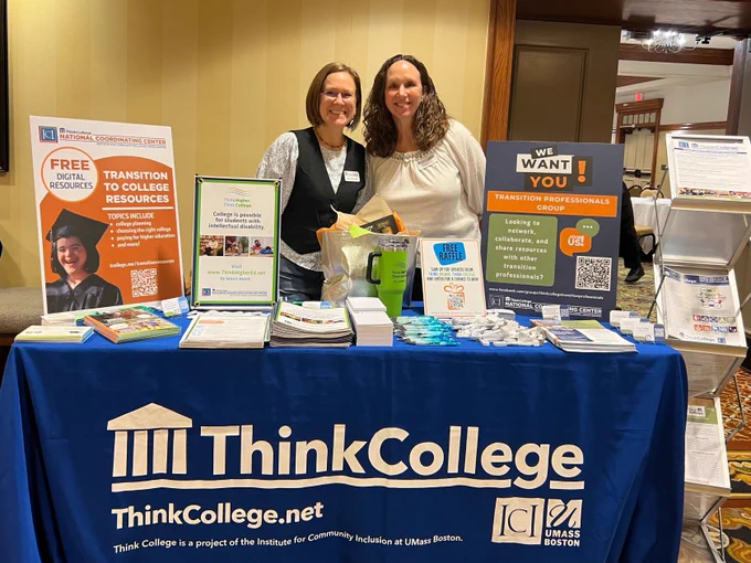 Two white women standing behind a Think College display. 