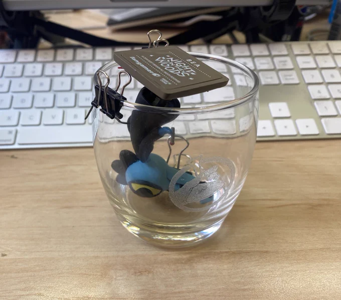 A figurine of Bea from Night in the Woods, upside down in a glass. The figurine is held in place with clips and wire, to help the glue dry correctly.