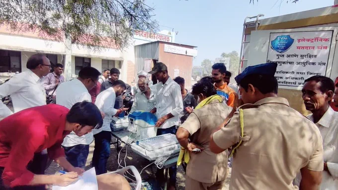 वरील फोटो मध्ये मतदान केंद्रस्तरीय अधिकारी EVM मशीन सोबत उभे आहे आणि त्यांच्या भोवती जमलेल्या गर्दीतील लोकांना ते evm मशीन बद्दल माहिती देत आहे सोबतच प्रात्याक्षिक सुरू आहे