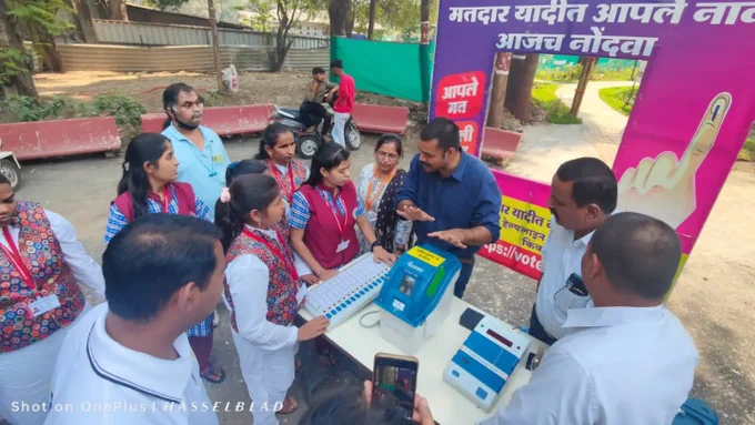 वरील फोटो मध्ये मतदान केंद्रस्तरीय अधिकारी EVM मशीन घेवून उभे आहे त्यांच्या समोर महाविद्यालयाच्या विद्यार्थींनी उभे आहे त्यांना मतदान केंद्रस्तरीय अधिकारी evm मशीन बद्दल माहिती देत आहे सोबतच प्रात्याक्षिक सुरू आहे.  