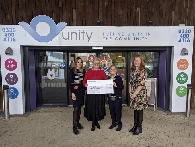 Image shows Unity CEO Terry Bishop stood outside the front of the Unity Office in Andover with two ladies from Nationwide who presented the cheque and Wendy Masterson, Unitys community business manager. She is holding a large cheque for £60,000 and everyone is smiling in to the camera.