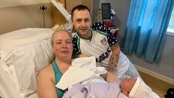 Kirsty Hind and Darren Cuthbertson with baby Reggie James, in a lilac blanket. Darren wears a Sunderland top and they are pictured in Kirsty's maternity room.