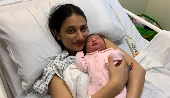 Armandeep Kaur, pictured holding her baby girl, who is wearing pink. She is resting in her hospital bed.
