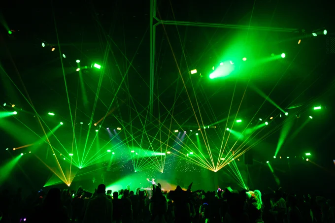 An upward-facing shot of green lights and lasers forming intricate, criss-crossing diagonal patterns and shapes in the Anthrocon Main Events ballroom as a crowd dances underneath.