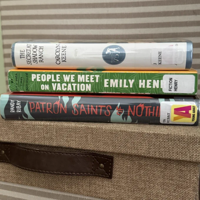 Stack of books: Nancy Drew The Secret at Shadow Ranch, The People We Meet on Vacation, Patron Saints of Nothing.