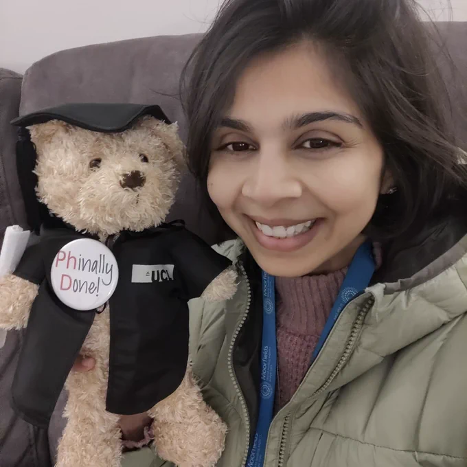 Image showing Dr. Shruti Chandra smiling brightly with a UCL graduation teddy bear dressed in a graduation cap and gown and holding a scrolled certificate. A badge with the words Phinally Done! is pinned onto the teddy bear.