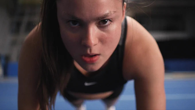 A close-up of a girl doing a push up, looking into the camera with a stern expression on her face.