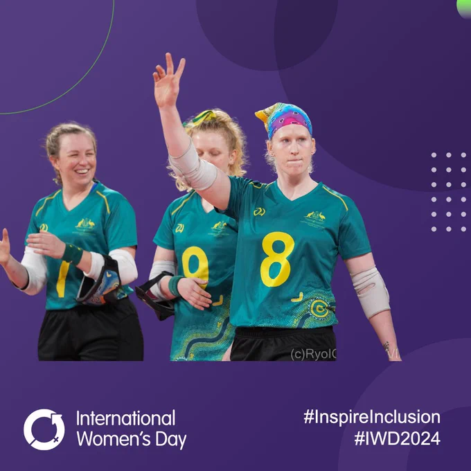 Three female goalball players from Australia stand together during a team presentation. One has raised her arm as her name is called