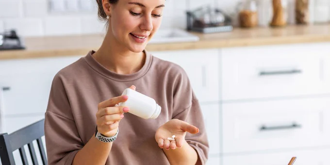 Adult woman shakes pills from a bottle onto her palm.