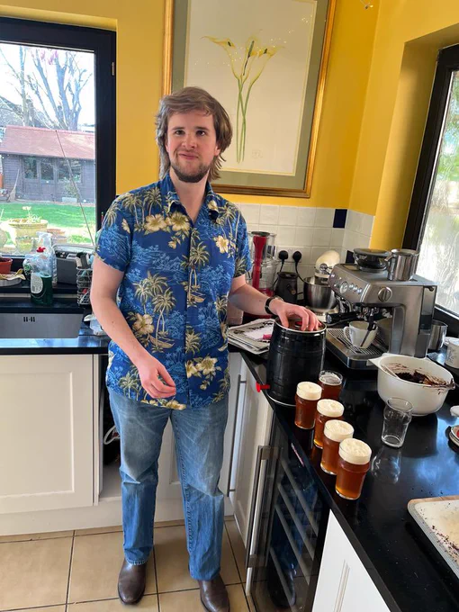 Me wearing a Hawaiian shirt filling a glass from a keg on the kitchen counter. There’s a row of half pint glasses next to the keg. Brackets, there are two photos and I’m not sure which ones which, so I’m just assuming this is the correct description.
