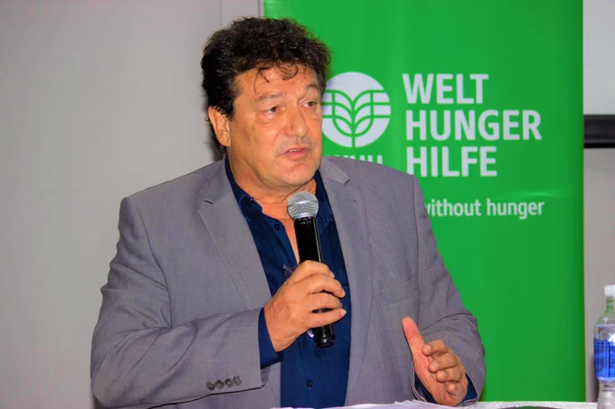 Man speaks on a microphone in front of a green Welthungerhilfe banner 