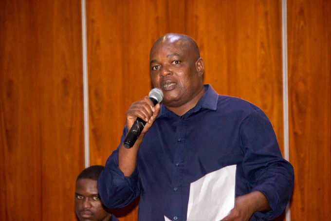Man dressed in a blue shirt holds and speaks into a microphone