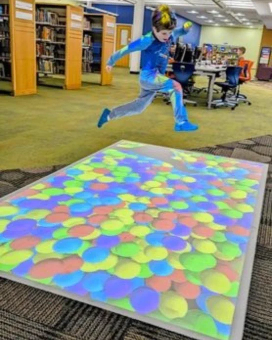 A young boy leaps in the air above the interactive floor projection of a colorful ball pit in Kids' World.