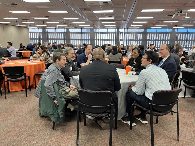 People of various genders and races gathered around tables in a conference room 
