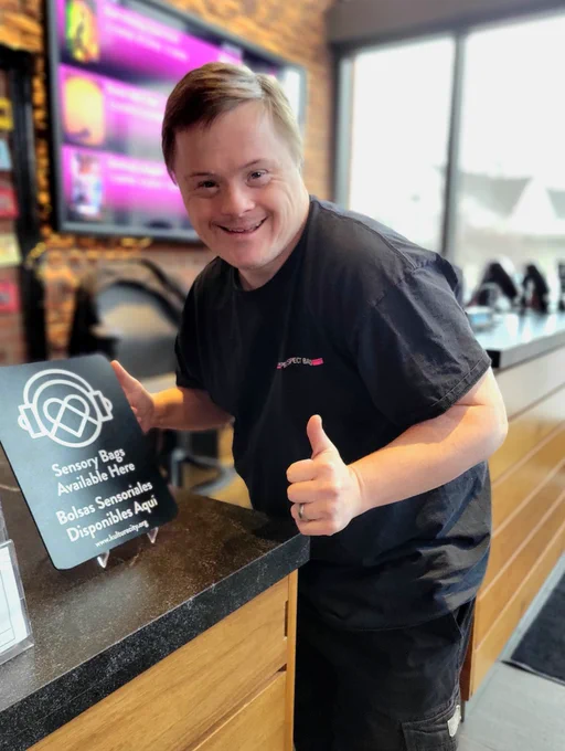 KMann gives a thumbs up next to a sign at Box Office that says Sensory Bags Available Here.