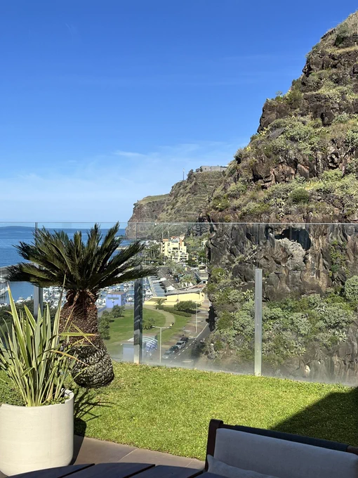 View of bright blue sky and sea next to the marina and green mountains of Calheta, Madeira.
