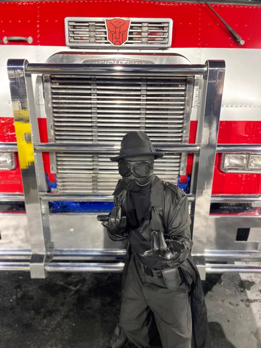 Figure in Spider-Man noire costume stood infront of an Optimus Prime Lorry