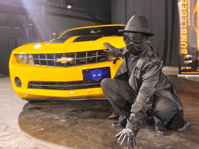Figure dressed as Spider-Man Noire, crouched next to a yellow Transformers movie Bumblebee style vehicle