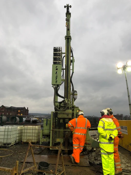 A group of people in PPE stand around a borehole drilling rig. 