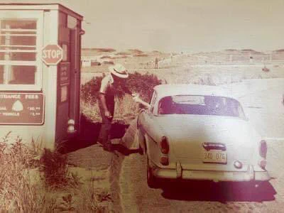 Historic image of 1950s style car paying an entrance fee to a park ranger at a beach fee booth.
